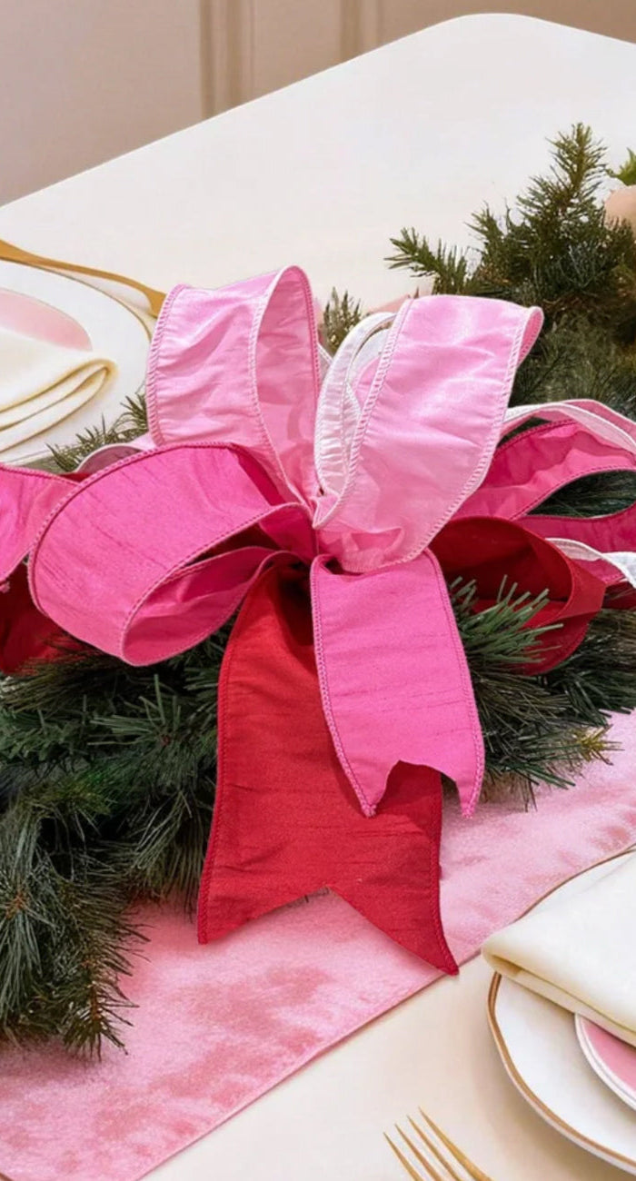 green pine garland, pink/red satin bow, pale roses. Festive dining.