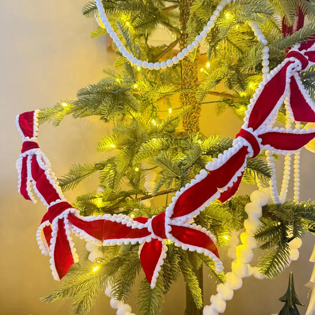Christmas tree adorned with red velvet ribbons (white pom-pom trim), white pom-pom garlands & warm fairy lights—cozy festive decor.