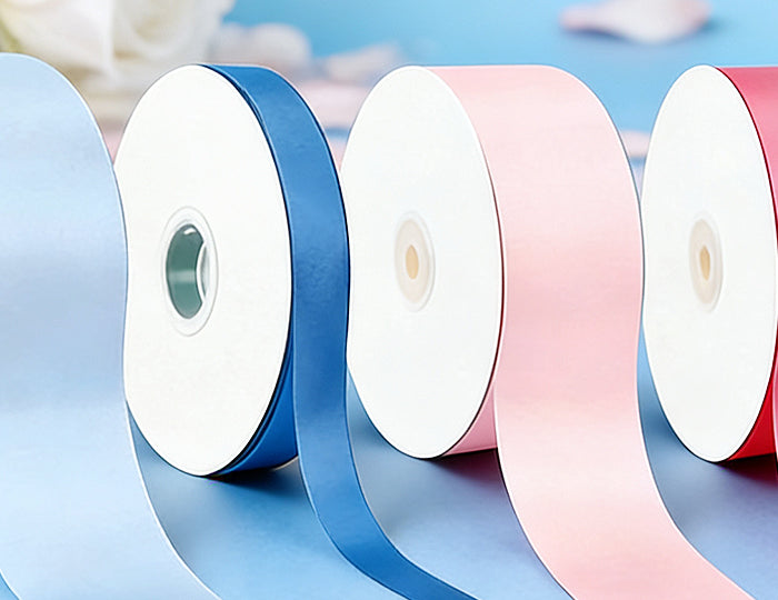 Satin ribbon rolls (blue, pink, red) on light blue background with petals – for crafts & decor