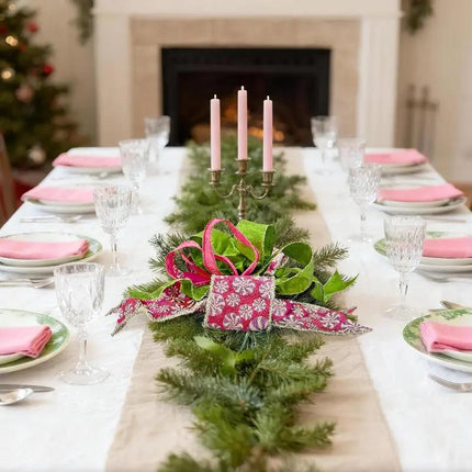 Christmas table centerpiece with pink peppermint-patterned, green & pink ribbons and pine branches, enhancing holiday dining ambiance.