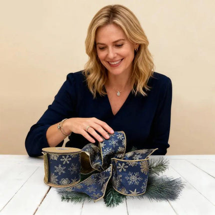 A woman crafting with navy blue and gold snowflake 4" wired jacquard ribbon, ideal for creative holiday projects.