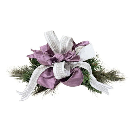 A Christmas decor piece has green pine branches with purple ribbons and silver-embroidered white ribbons.