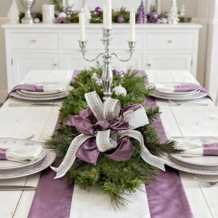A Christmas table centerpiece has pine foliage with purple and silver-embroidered white ribbons.