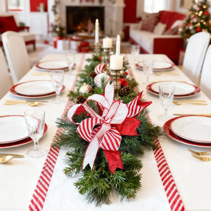 A Christmas dining table has a pine centerpiece with red-white striped, pom-pom-trimmed, and solid red ribbons.