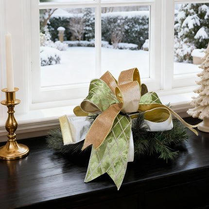 Festive Christmas decor with a large bow (green, gold, white) on pine greenery, gold candlestick, and snowy window view.