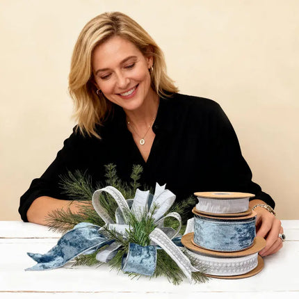 Woman crafting a Christmas centerpiece with pine and blue/silver ribbons, ideal for festive decor and DIY holiday crafts.