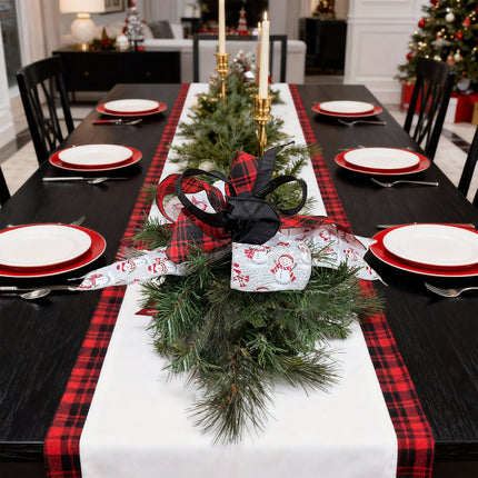 Christmas dining table with red/black plaid runner, snowman ribbon bow, green pine, festive setup.