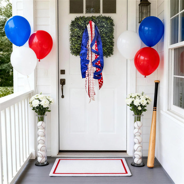 Baseball-themed front door wreath with royal blue dupioni, baseball print, and red polka dot ribbons, paired with red, white, and blue balloons