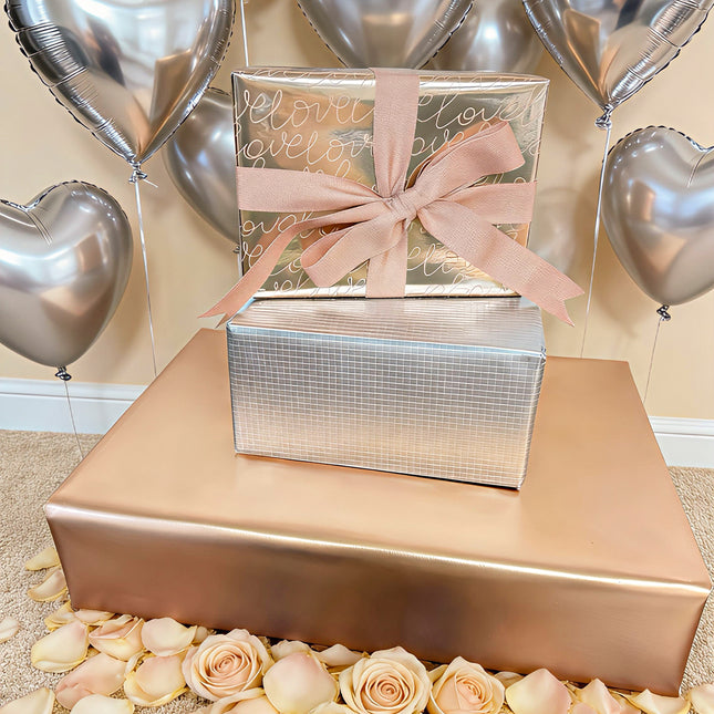 Gifts wrapped in metallic paper (silver grid/rose gold "love") + bow; romantic gifting.