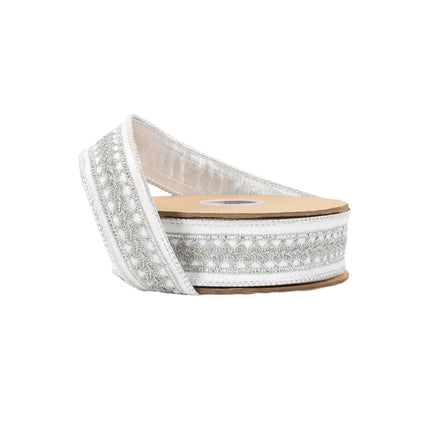 A spool of ribbon features a white base with intricate silver embroidered patterns and metallic accents.
