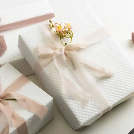Textured white gift boxes styled with frayed chiffon ribbon bows and floral accents, ideal for elegant gifting.