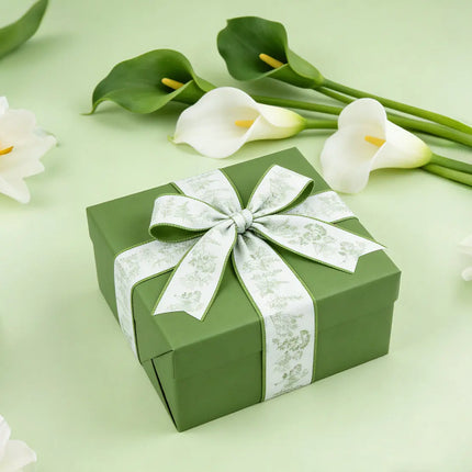 Green gift box with a white herb print wired ribbon bow, surrounded by white calla lilies for fresh spring gift wrapping decor.