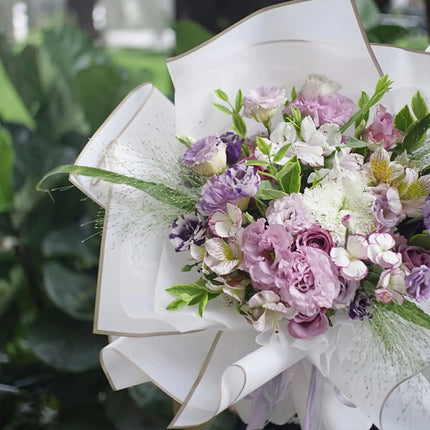 Romantic pastel bouquet with pink and purple blooms, wrapped in premium white matte floral sheets with gold trim