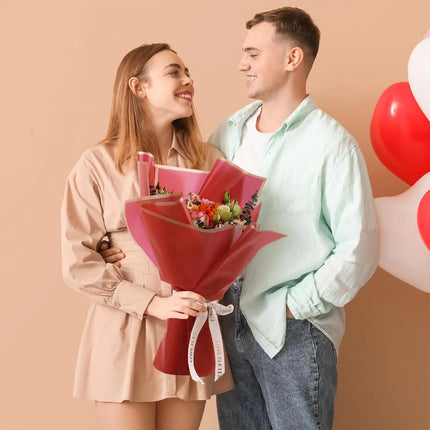 Romantic moment of a couple exchanging a vibrant bouquet wrapped in 58x58cm Red Matte Floral Sheets with Gold Edge