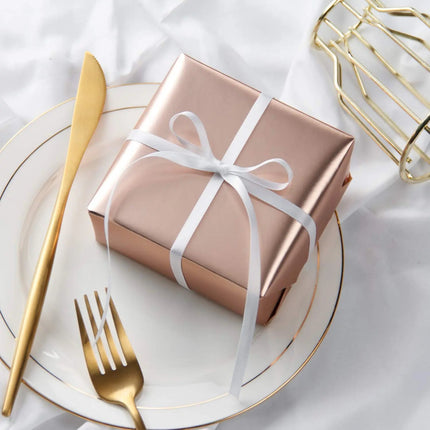 Rose gold matte-wrapped gift + white satin bow; formal event gifting.