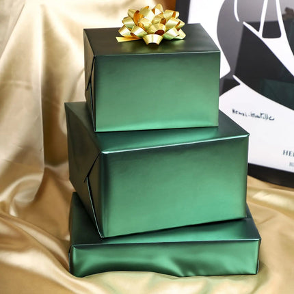 Stacked matte green wrapped gift boxes with gold bow, perfect for holiday gift presentation.